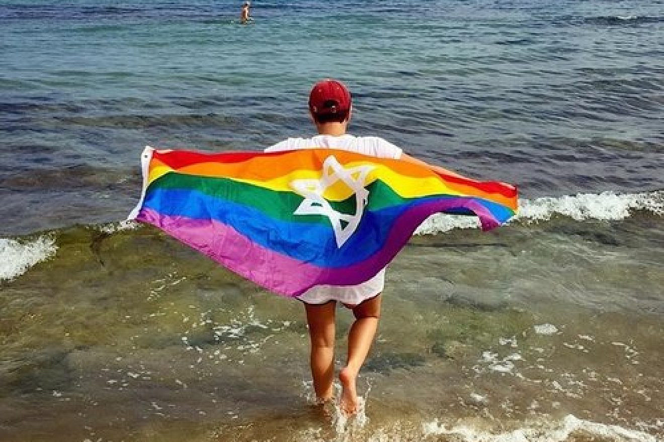 A Birthright Israel trip participant with a Jewish gay-pride flag parade on the Hilton Beach in Tel Aviv. Credit: Birthright Israel Facebook page.