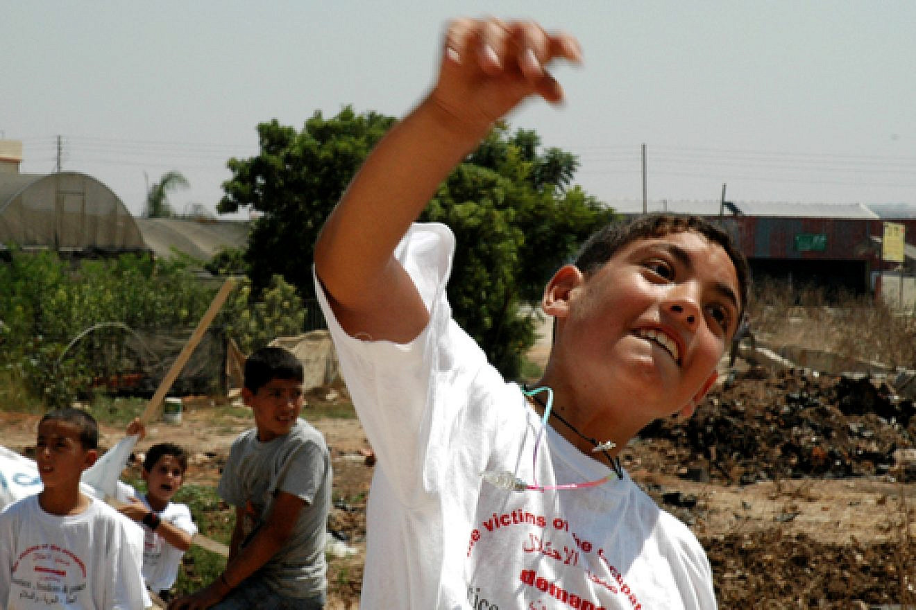 Click photo to download. Caption: A Palestinian boy throws a stone at Israel's security fence. Credit: Justin McIntosh.