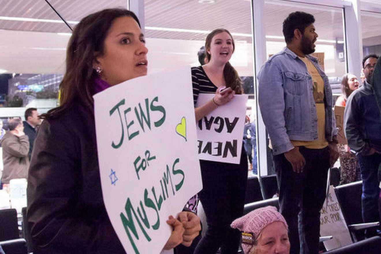 At left, a protester at San Francisco International Airport holds a sign reading “Jews For Muslims” during a demonstration against the Trump administration’s temporary travel ban affecting Muslim-majority countries Jan. 29, 2017. Credit: Kenneth Lu via Wikimedia Commons.