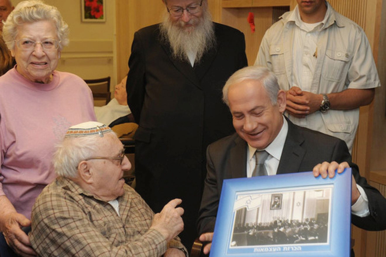 In April 2012, Israeli Prime Minister Benjamin Netanyahu visits senior citizens living at a retirement home in Jerusalem, showing them a picture of David Ben-Gurion's announcement of Israeli independence at Tel Aviv's Independence Hall on May 14, 1948. Credit: Amos Ben Gershom/GPO/Flash90.