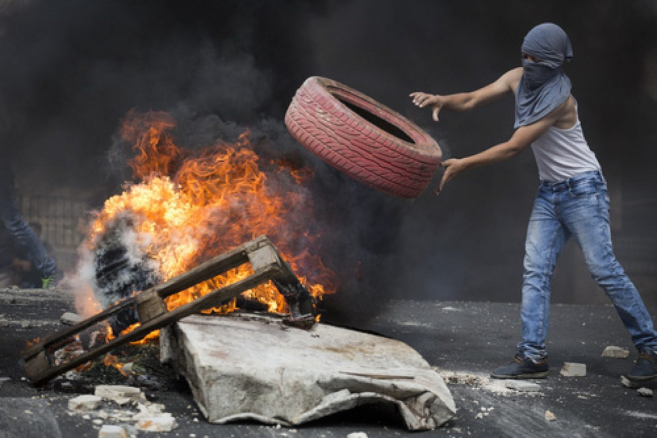 Click photo to download. Caption: On Oct. 7, 2015, a Palestinian rioter throws a tire into a fire, blocking a road during clashes with Israeli police in eastern Jerusalem. Credit: Hadas Parush/Flash90.