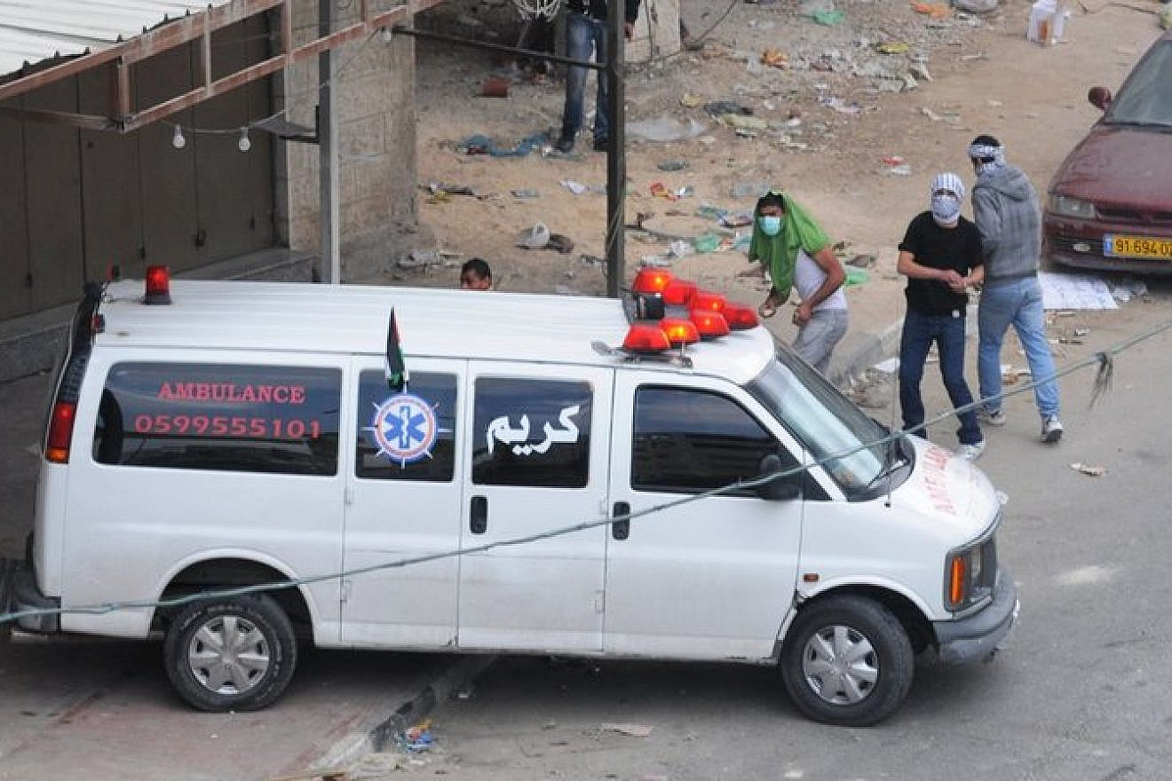 Palestinians throw rocks from behind an ambulance during a riot in Qalandiya. Credit: IDF.