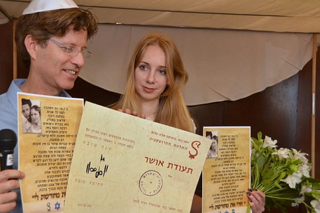 Boaz Bau-Simon, the grandson of Joseph and Rebecca Bau, with his fiancé Or (Irena) Gatina in February 2014. The couple announced its engagement at the ceremony commemorating the 70th wedding anniversary of Bau-Simon's grandparents. Bau-Simon and Gatina are pictured holding a "teudat osher" ("certificate of happiness") originally created by Joseph Bau as well as a letter relating the story of the lifelong romance of Joseph and Rebecca Bau. Credit: Maxine Dovere.