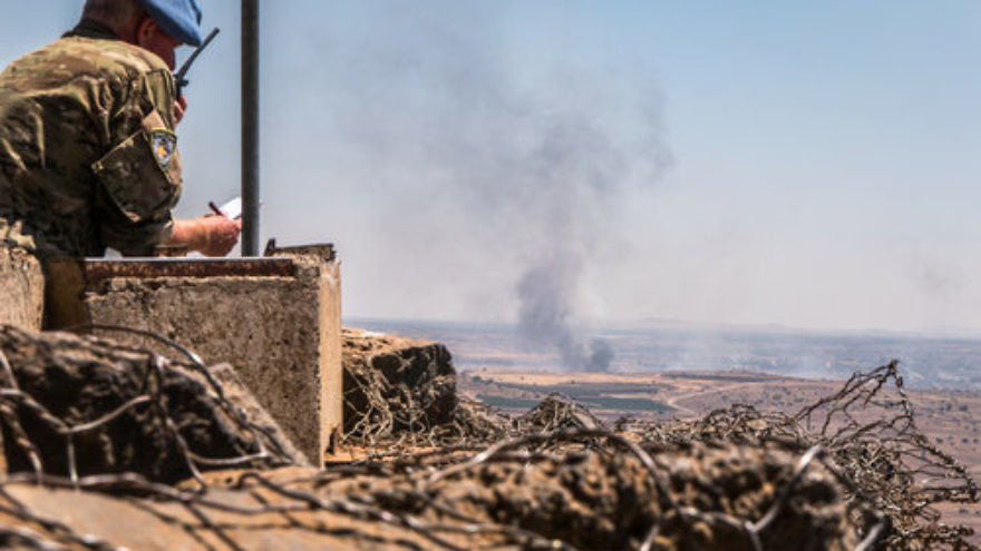 A U.N. observer is stationed at a lookout point as smoke rises in a Syrian village near the Israel border in the Golan Heights during fighting in the Syrian civil war, June 25, 2017. Credit: Basel Awidat/Flash90.