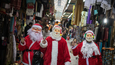 People dressed up as Santa Claus walk through the market in Jerusalem’s Old City on Christmas eve, Dec. 24, 2017. Credit: Hadas Parush/Flash90.