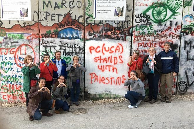 Members of the Presbyterian Church USA's Israel Palestine Mission Network pose in front of Israel's security barrier during one of their trips to the Holy Land. The graffiti on the barrier readers “PC(USA) stands with Palestine.” Credit: Twitter.