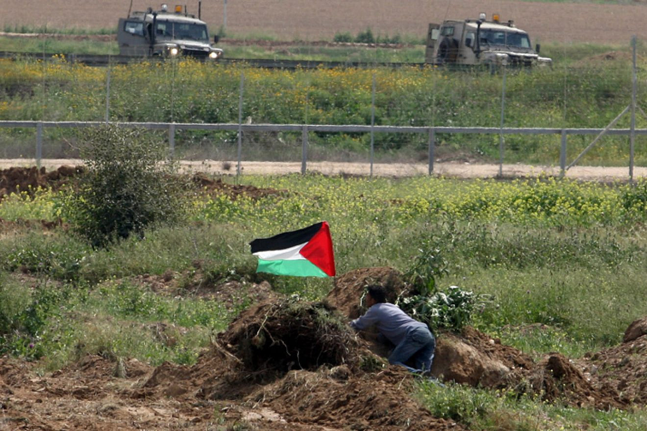 A Palestinian man waves the Palestinian flag near Israeli soldiers by the border fence near Gaza City in March 2010. Photo by Wissam Nassar/Flash90.