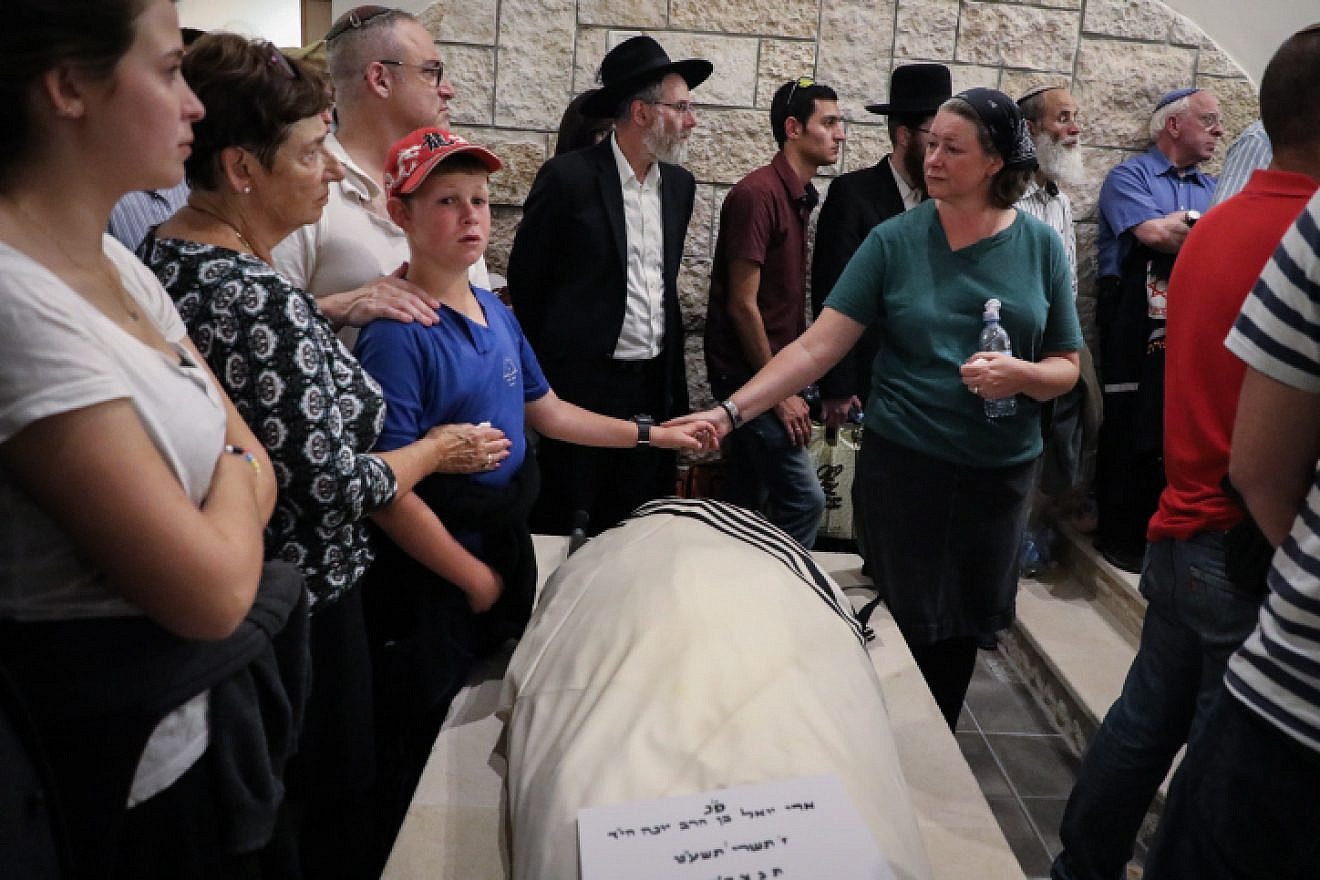 Ari Fuld's wife, Miriam, and son hold hands over his enshrouded body, wrapped in a tallit and awaiting burial at the Kfar Etzion cemetery in Judea. Photo by Gershon Elinson/Flash90.