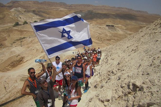 Birthright Israel participants hike up Masada, Israeli flag in hand. Credit: Courtesy.