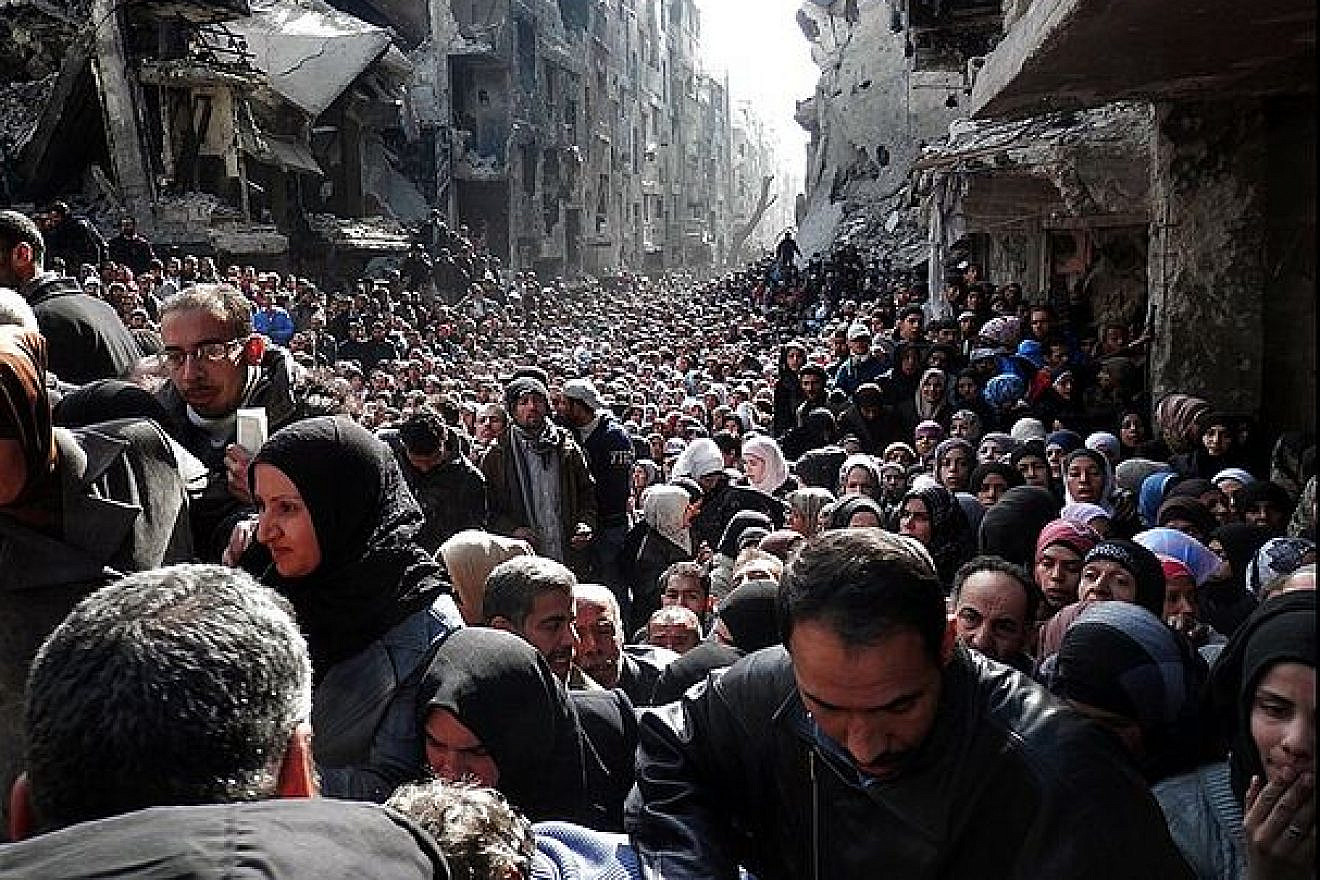 Thousands of Syrian and Palestinian refugees queue for food in the Yarmouk camp in Syria on February 2014. The camp today is a pile of rubble. Credit: UNRWA via Wikimedia.