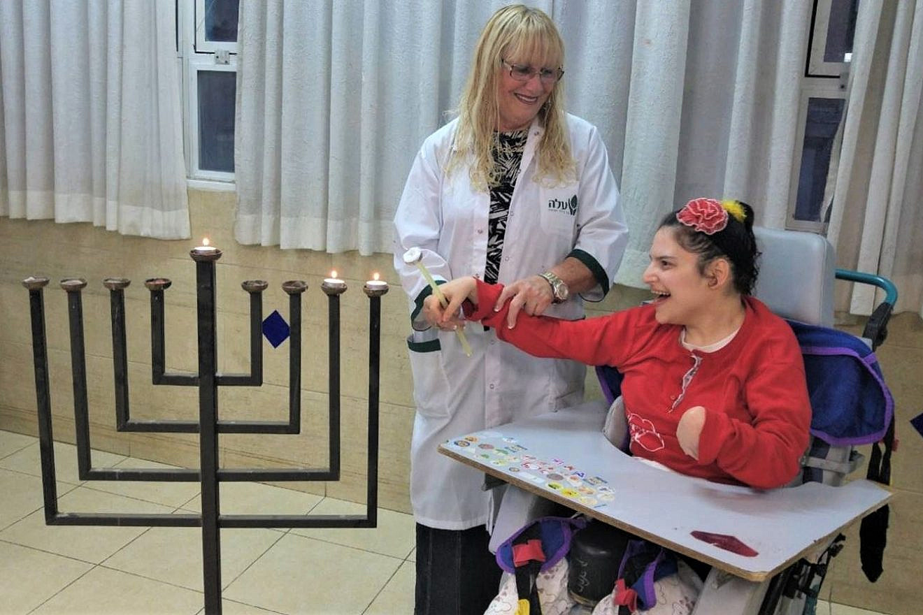 A young woman at ALEH lights the Hanukkah menorah with help from a staff member. Credit: ALEH.