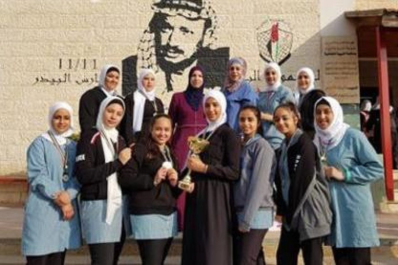 Palestinian girls pose in front of their school in Bethlehem on Nov. 19, 2019. Visible on the wall by the school entrance is a plaque honoring Ayat al-Akhras, an 17-year-old suicide bomber that killed two Israelis in 2002. Credit: Palestinian Media Watch.