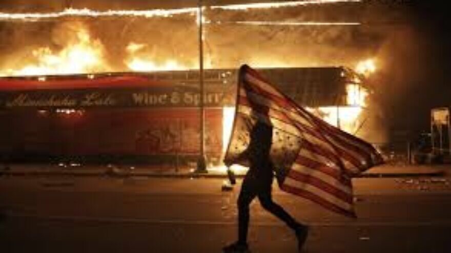 A protester flies an upside-down American flag through the streets of one of the cities beset by riots in the wake of the killing of George Floyd by Minneapolis police officers on May 29, 2020. Source: Screenshot.