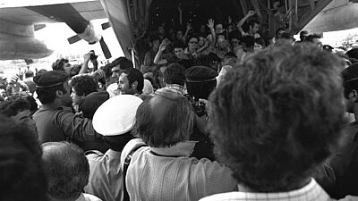 Rescued Air France passengers wave to the waiting crowd while leaving the belly of the Hercules plane at Ben-Gurion International Airport. Credit: Moshe Milner, July 4, 1976, from National Photo Collection of Israel, Photography Department, Government Press Office via Wikimedia Commons.