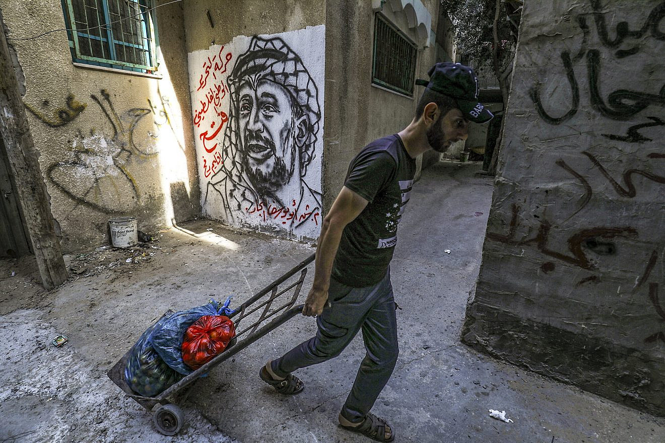 A Palestinian dragging bags of fruit passes a mural depicting late Palestinian leader Yasser Arafat in Rafah, in the southern Gaza Strip, on Nov. 11, 2021. Photo by Abed Rahim Khatib/Flash90.