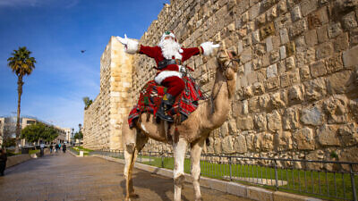 Issa Kassissieh, dressed as Santa Claus, rides a camel in Jerusalem's Old City, during Christmas a tree distribution and a few days before the upcoming holiday of Christmas, December 23, 2021. Photo by Olivier Fitoussi/Flash90