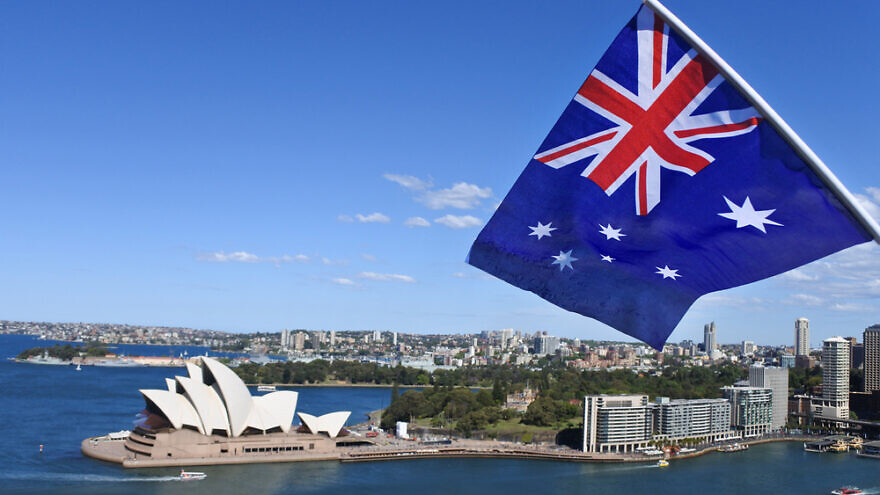 The national flag of Australia flies above the Sydney Harbor and the Opera House in. Credit: ChameleonsEye/Shutterstock.