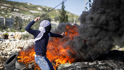A Palestinian youth launches rocks at Israeli security forces during a protest in the village of Kfar Qaddum, near the West Bank city of Nablus on March 13, 2021. Photo by Nasser Ishtayeh/Flash90.