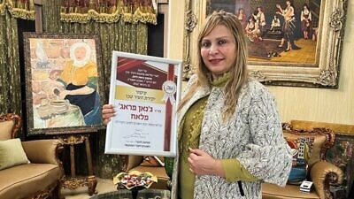 Dr. Janan Faraj Falah with her award from Akko City Hall. Her painting of a Druze woman is in the background. Photo courtesy of Janan Faraj Falah