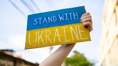 A demonstrator holds a “Stand with Ukraine” sign. Credit: Wachiwit/Shutterstock.