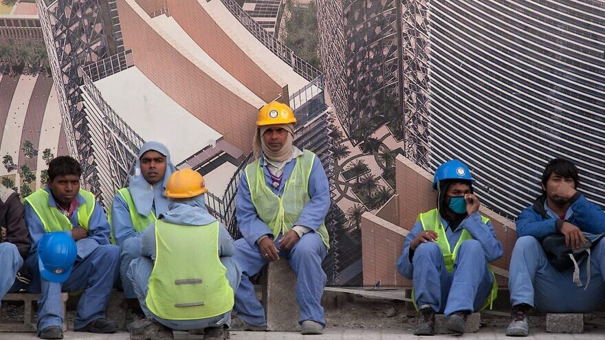 Migrant workers in the West Bay area of Doha, Qatar, waiting for a bus on Feb. 1, 2014. Credit: Alex Sergeev via Wikimedia Commons.