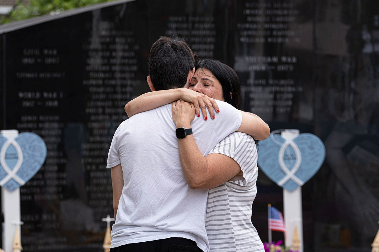 Two people embrace at the scene of a memorial for the seven people killed and 30 wounded by a 21-year-old gunman who opened fire at a July 4th parade in Highland Park, Ill., July 6, 2022. Credit: Willie Gillespie/Shutterstock.