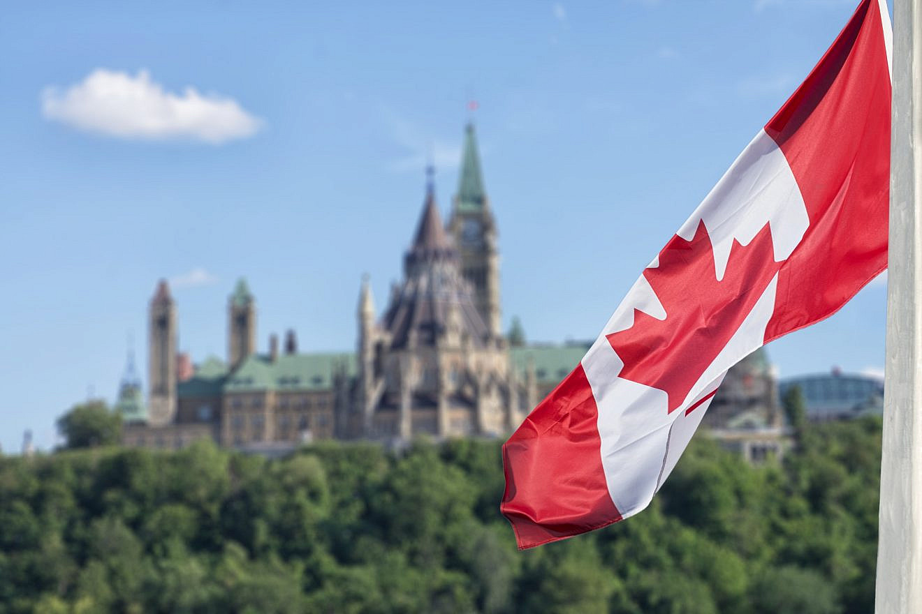 Canadian flag waving with Parliament buildings in the background. Credit: DD Images/Shutterstock.
