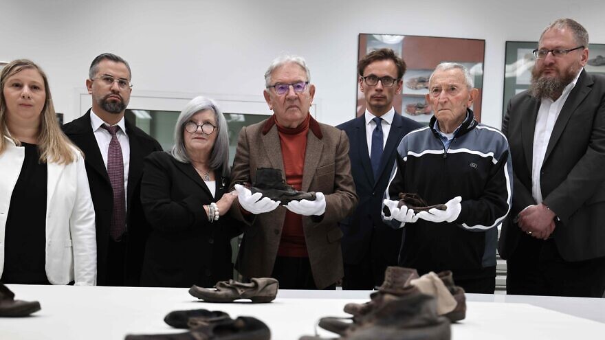Auschwitz survivors Arie Pinsker (left center), and Bogdan Barnikowski, (right center) hold the shoes of child victims of the Nazis in the Conservation Lab in Auschwitz, joined by representatives of March of the Living, the Neishlos Foundation, and the Auschwitz-Birkenau Foundation. Photo by Tali Natapov/Neishlos Foundation.