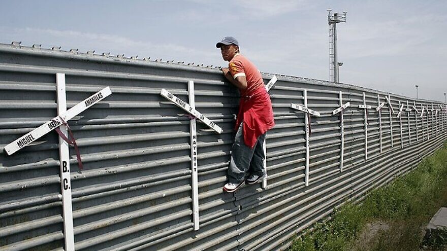 A migrant from Mexico scaling the border fence into the United States. Source: Wikimedia Commons.