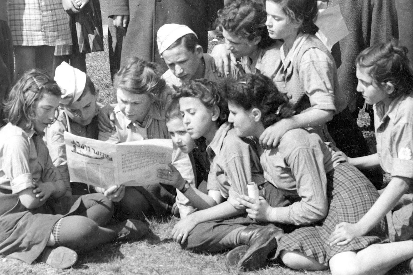 Children read a Yiddish newspaper as they await the train in Kaserne, Germany, during the post-war years. Credit: UN Archives, S-1058-0001-01-00175.