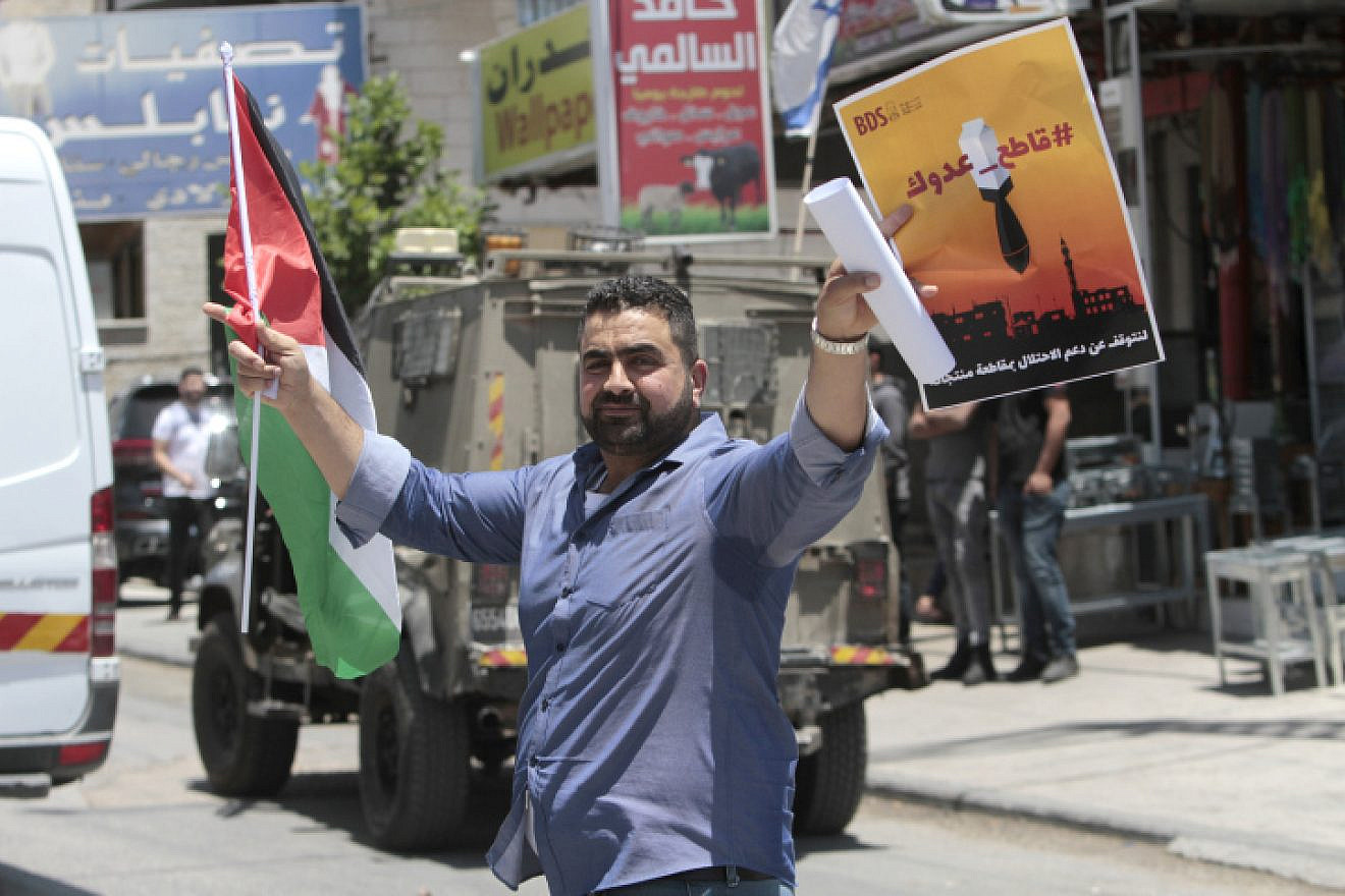 A Palestinian holds a PLO flag and a poster calling to boycott Israeli products during a demonstration in Huwara, south of Nablus, May 22, 2021. Photo by Nasser Ishtayeh/Flash90.