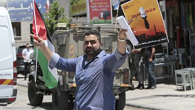 A Palestinian holds a PLO flag and a poster calling to boycott Israeli products during a demonstration in Huwara, south of Nablus, May 22, 2021. Photo by Nasser Ishtayeh/Flash90.