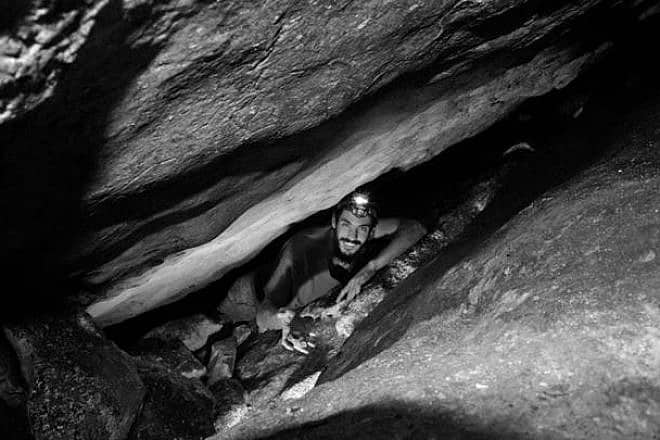 Extricating an oil lamp from a crevice between boulders. Photo by B. Zissu/ Te’omim Cave Archaeological Project.