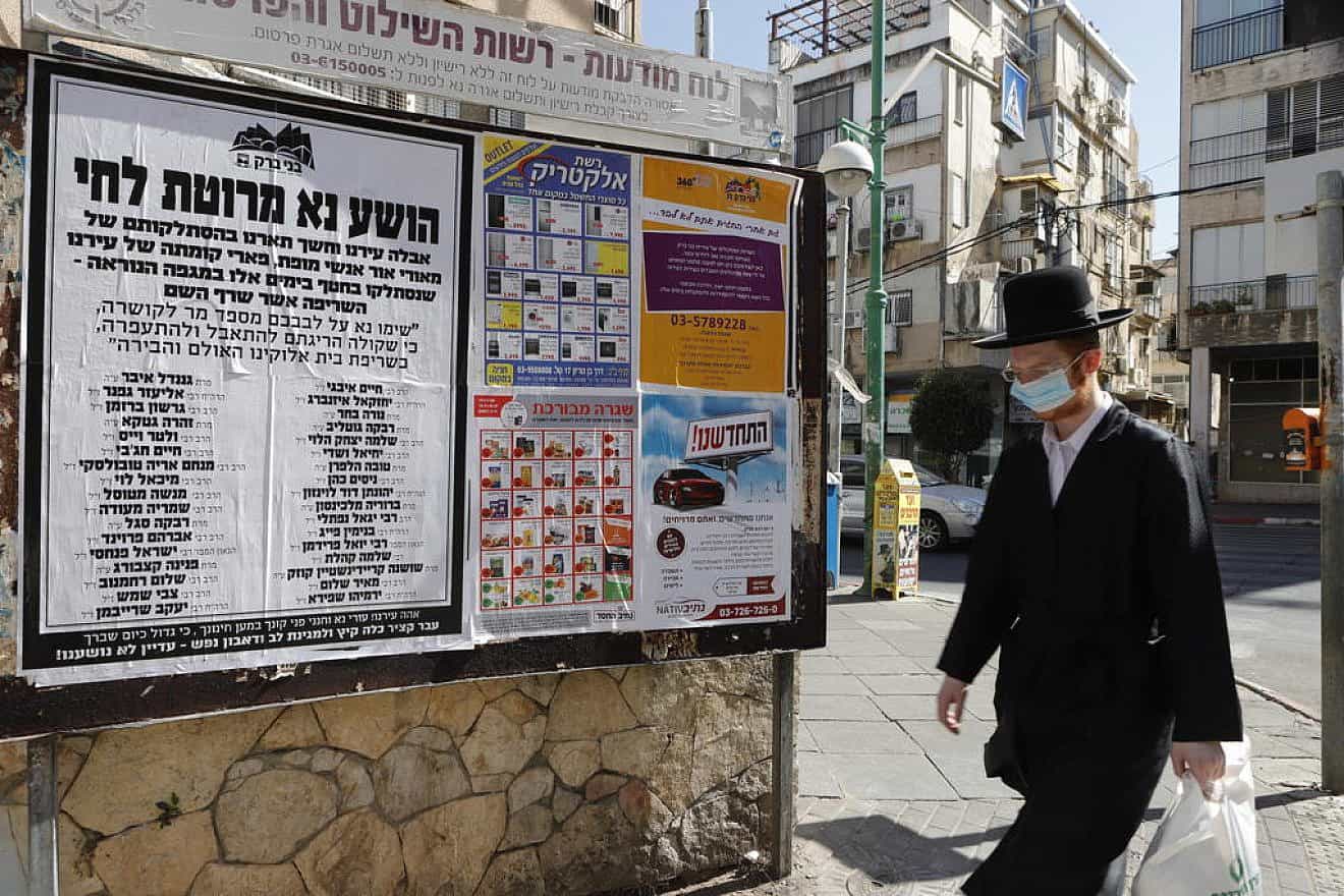 An man walks past a sign in Bnei Brak urging masking and social distancing, Oct. 16, 2020. Photo by Eitan Elhadez-Barak/TPS.