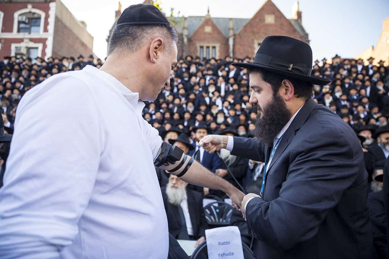 Rabbi Mendy Kotlarsky (right) wraps tefillin on a man as he awaits  a group picture in front of Chabad-Lubavitch world headquarters in Brooklyn on Nov. 4, 2018. Credit: Mendel Grossbaum/Chabad.org.