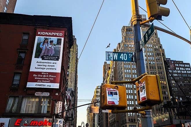 Posters depicting Israeli hostages that Hamas terrorists are holding in the Gaza Strip near a large billboard that the watchdog group CAMERA took out near the Midtown Manhattan offices of “The New York Times,” November 2023. Credit: Courtesy.