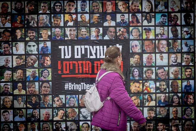 People walk next to pictures of civilians held hostage by Hamas terrorists in Gaza, in Jerusalem, Feb. 12, 2024. Photo by Chaim Goldberg/Flash90.